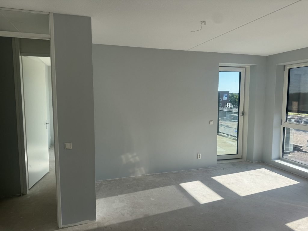 Lege nieuwbouwkamer met kale wanden, een betonvloer en zichtbare plafondnaden