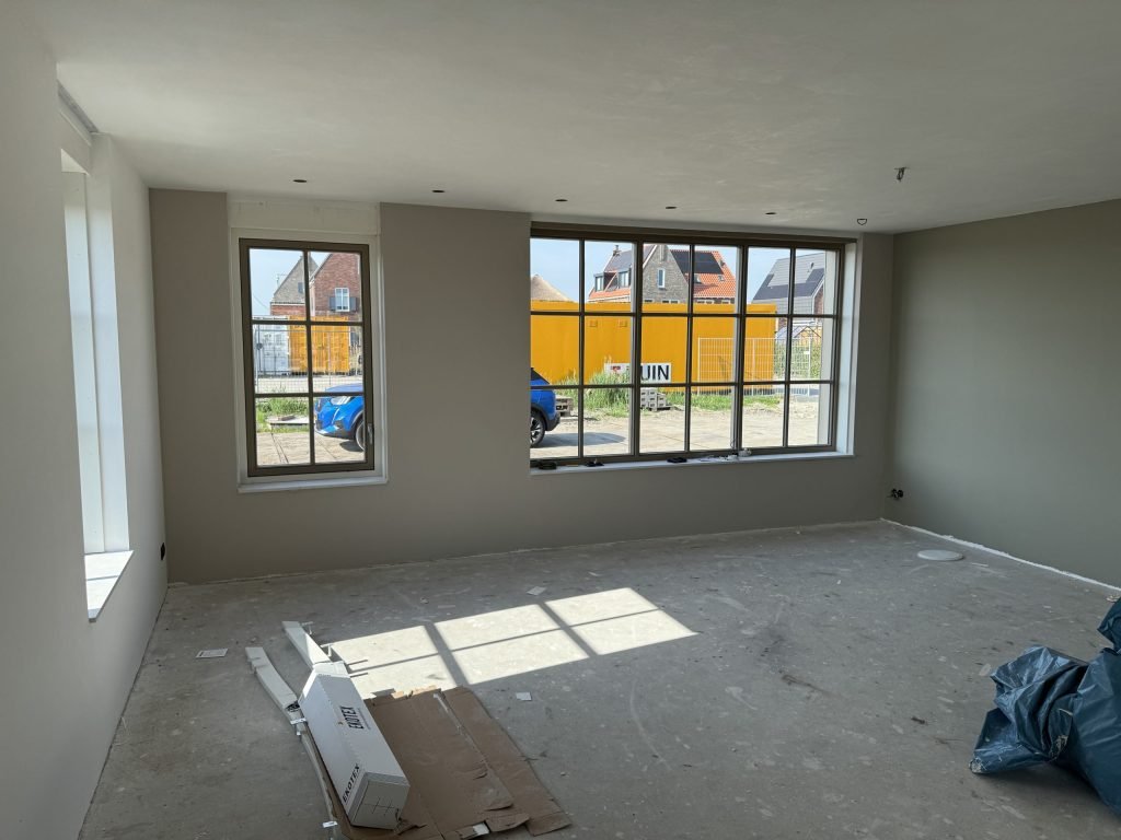 Lege nieuwbouwkamer met een kaal plafond, wanden in een warme grijstint en grote ramen